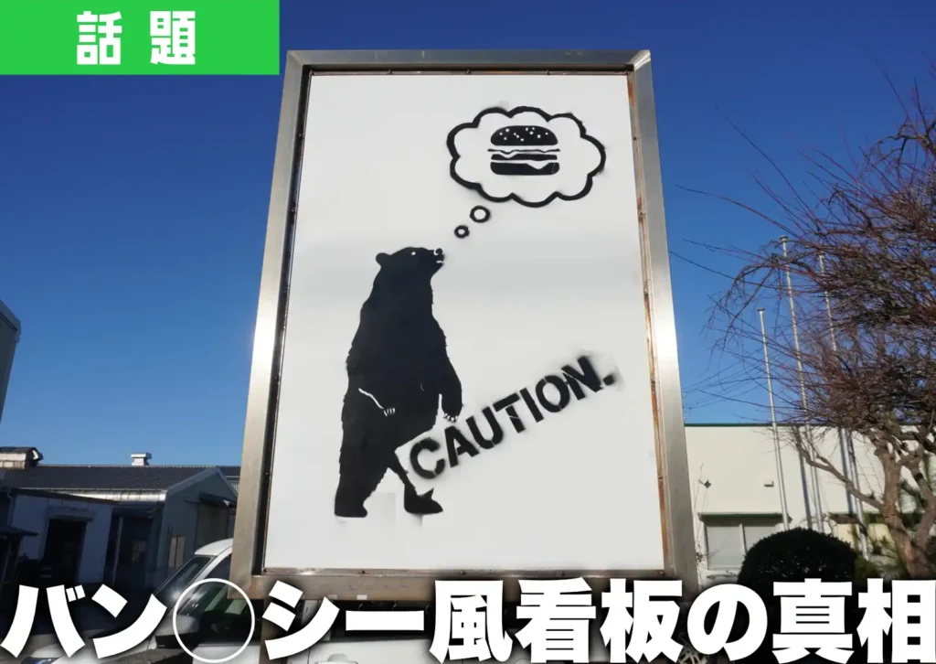 鶴岡市宝田にあるバンクシー風の看板。熊とハンバーガーの絵とともにCOUTIONと書かれている